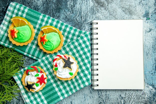 Vue de dessus petites tartes de Noël sur le bloc-notes de branches de pin nappe sur table grise