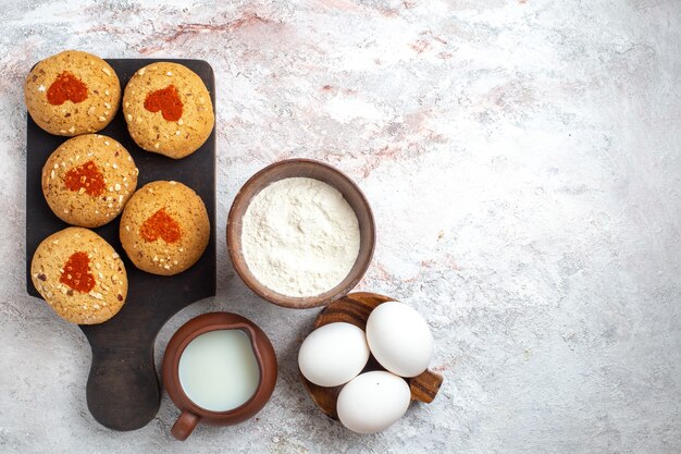 Vue de dessus petits biscuits au sucre délicieux bonbons pour le thé avec des œufs et du lait sur la surface blanche biscuit tarte biscuit sucre gâteau sucré