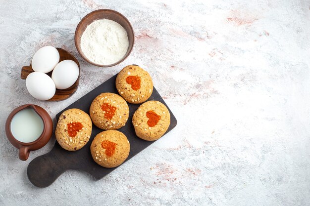 Vue de dessus petits biscuits au sucre délicieux bonbons pour le thé avec des œufs et du lait sur la surface blanche biscuit tarte biscuit sucre gâteau sucré