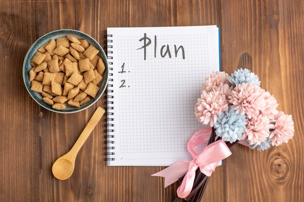 Vue de dessus petits biscuits d'oreiller avec bloc-notes et fleurs sur un bureau marron