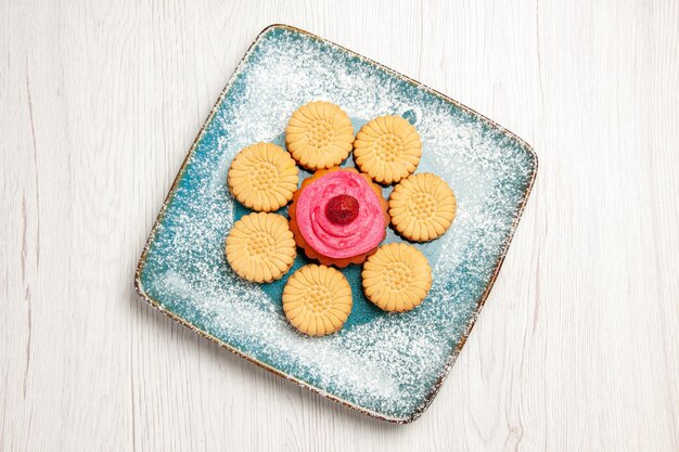 Vue de dessus de petits biscuits sucrés avec gâteau aux fruits à l'intérieur de la plaque sur un tableau blanc