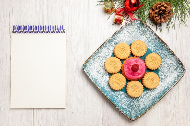 Vue de dessus de petits biscuits sucrés avec gâteau aux fruits à l'intérieur de la plaque sur un tableau blanc