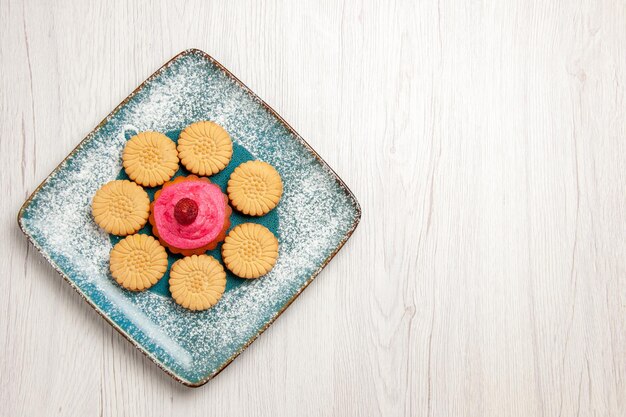 Vue de dessus de petits biscuits sucrés avec gâteau aux fruits à l'intérieur de la plaque sur un tableau blanc