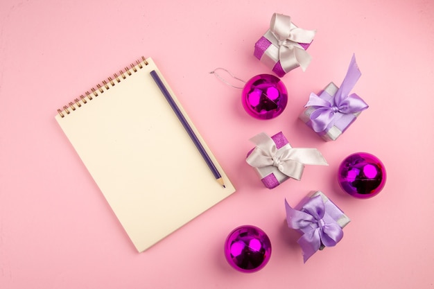 Vue de dessus de petits cadeaux avec bloc-notes et jouets sur surface rose