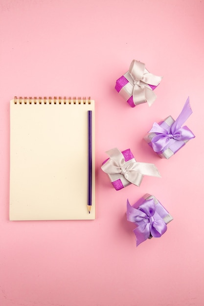 Vue de dessus de petits cadeaux avec bloc-notes sur la surface rose