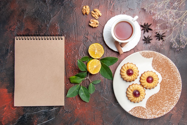 Vue de dessus petits cookies avec tasse de thé sur le gâteau biscuit au sucre de table sombre