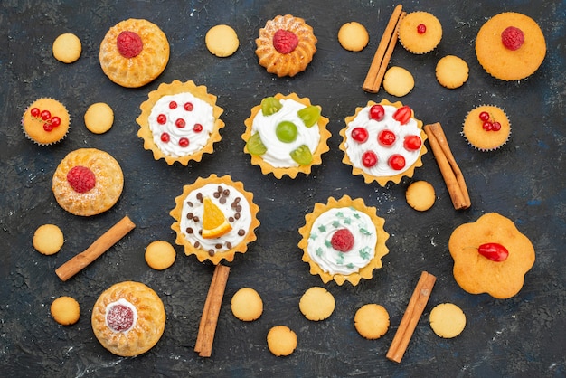 Vue de dessus petits gâteaux à la crème avec des biscuits et de la cannelle sur le dessert de biscuit de surface sombre