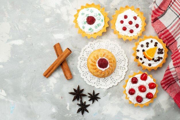 Vue de dessus petits gâteaux à la crème de cannelle et de différents fruits isolés sur la surface légère sucre sucré