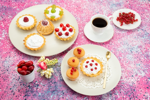 Vue de dessus petits gâteaux à la crème de fruits frais et avec une tasse de café à l'intérieur d'une plaque blanche sur le bureau lumineux