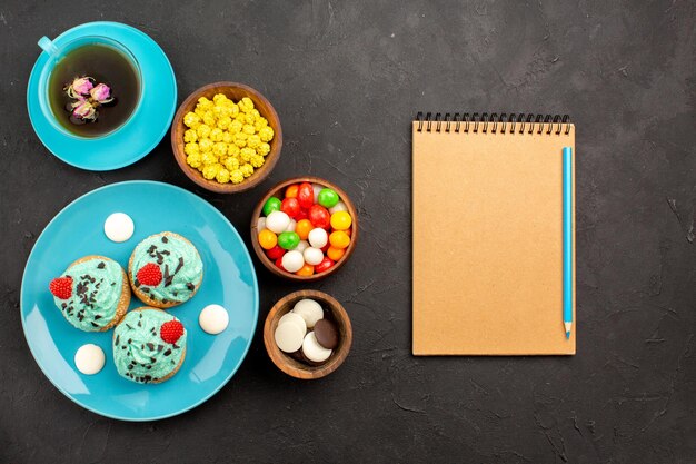 Vue de dessus petits gâteaux crémeux avec tasse de thé et bonbons sur la surface sombre gâteau à la crème de thé biscuit dessert couleur