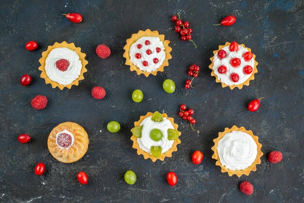 Vue de dessus petits gâteaux délicieux avec de la crème et des fruits frais sur le fruit du bureau noir