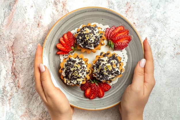 Vue de dessus de petits gâteaux délicieux avec des fraises sur une surface blanche fête d'anniversaire gâteau aux biscuits sucrés