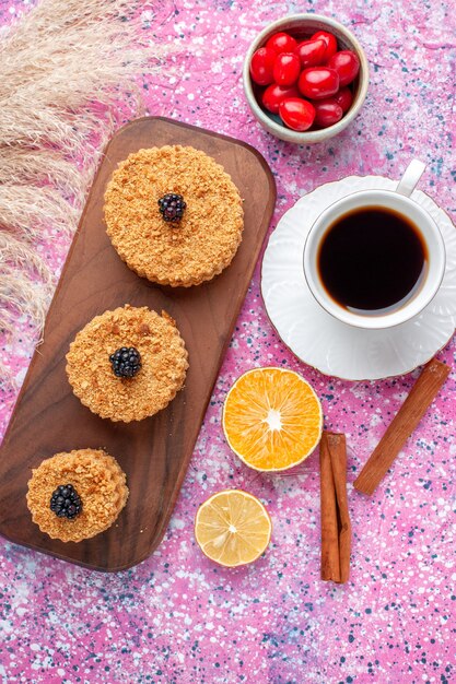 Vue de dessus de petits gâteaux délicieux ronds formés avec de la cannelle et du thé sur la surface rose clair