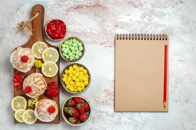 Photo gratuite vue de dessus de petits gâteaux sucrés avec des tranches de citron et des bonbons sur fond blanc gâteau aux agrumes frais biscuit sucré