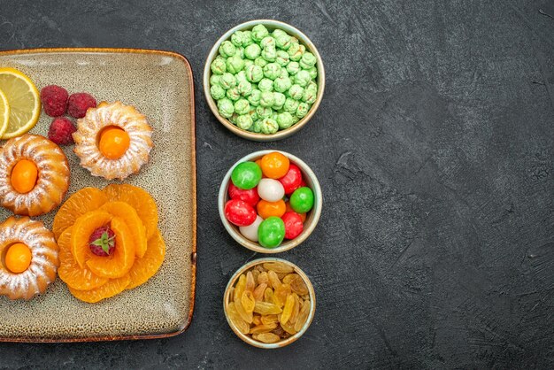 Vue de dessus de petits gâteaux avec des tranches de citron mandarines et bonbons sur fond noir