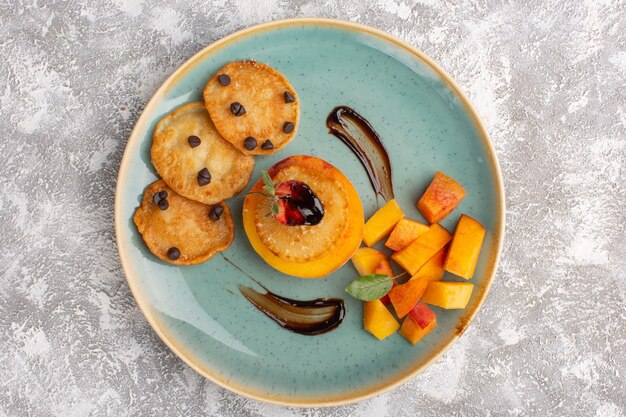 Vue de dessus peu de pâtisseries cookie à l'intérieur de la plaque avec des pêches en tranches fraîches sur table lumineuse, gâteau biscuit pâtisserie au sucre cuire