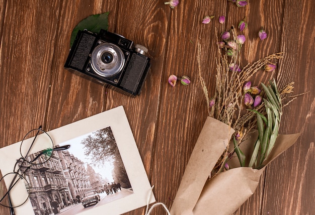 Vue de dessus de la photo et des lunettes vieil appareil photo avec des branches sèches de couleur blanche dans du papier kraft et des boutons de rose secs éparpillés sur du bois