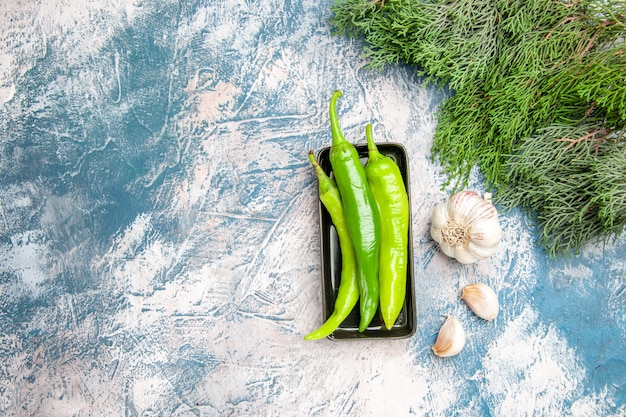 Vue de dessus des piments verts sur l'ail de la plaque noire sur fond bleu-blanc