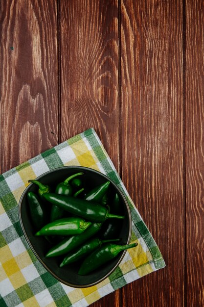 Vue de dessus de piments verts frais dans un bol sur une serviette à carreaux sur fond rustique en bois avec copie espace