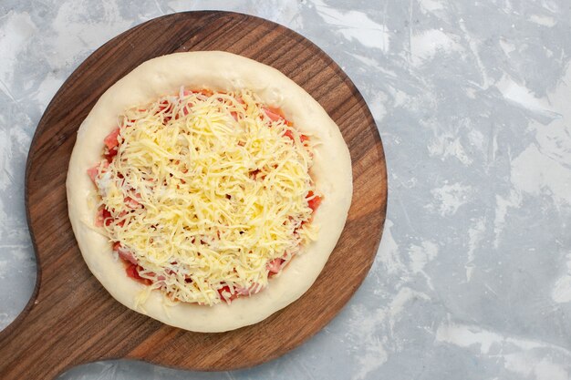 Vue de dessus de la pizza crue avec du fromage avant d'aller au four sur blanc