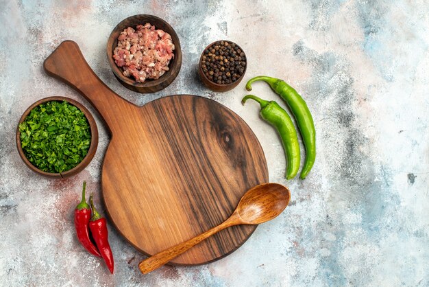 Vue de dessus une planche à découper une cuillère en bois bols avec des légumes de viande poivre noir piments forts sur fond nu espace libre