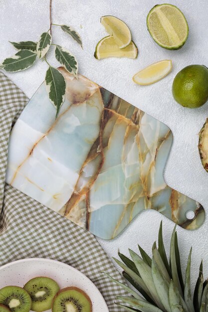 Vue de dessus de la planche à découper sur un tissu à carreaux avec de la chaux et du kiwi avec des feuilles d'ananas sur fond blanc