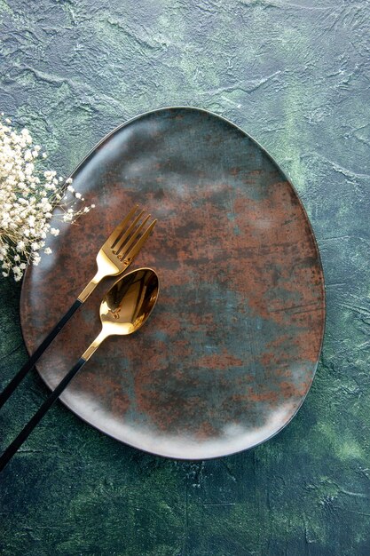 Vue de dessus plaque brune avec une cuillère et une fourchette d'or sur une surface sombre couleur des aliments restaurant ustensiles de cuisine couverts repas dîner