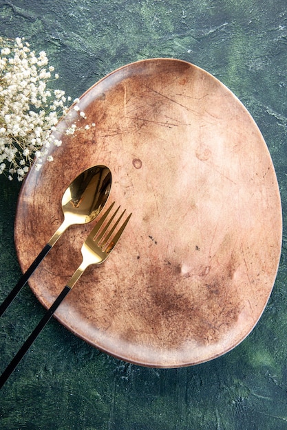 Vue de dessus plaque brune avec cuillère et fourchette en or sur une surface sombre dîner couverts repas nourriture restaurant table de couleur des ustensiles