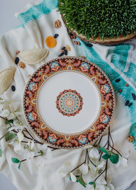 Photo gratuite vue de dessus de la plaque orientale en céramique avec un motif national avec shekerbura et semeni sur le mur de l'écharpe féminine en soie traditionnelle kelagai blanc