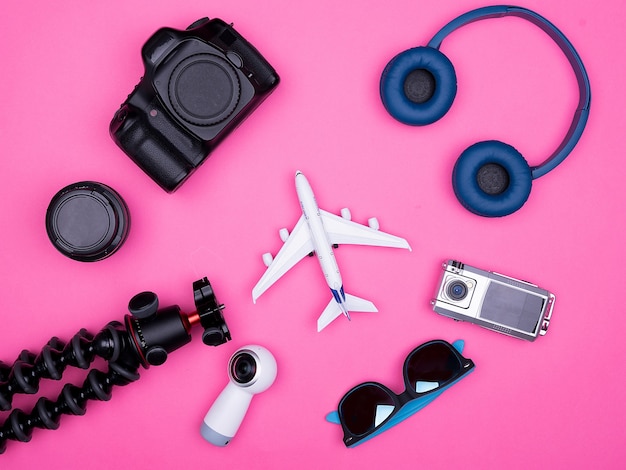 Vue de dessus à plat des accessoires de photographe de voyage sur fond rose. écouteurs trépied. des lunettes de soleil