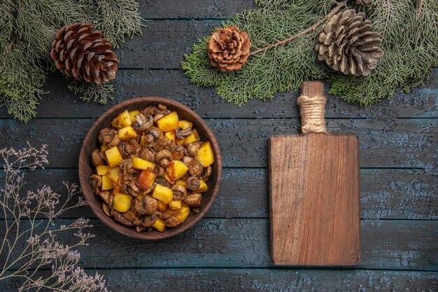 Vue de dessus plat et planche bol de pommes de terre et de champignons à côté de la planche coupée sous les branches d'épinette avec des cônes