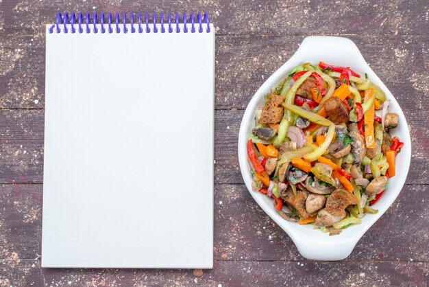 Vue de dessus plat de viande en tranches avec des légumes cuits à l'intérieur de la plaque avec bloc-notes sur le fond en bois brun plat de viande de légumes