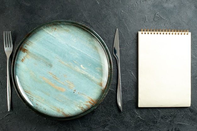 Vue de dessus plateau rond couteau et fourchette cahier sur table noire
