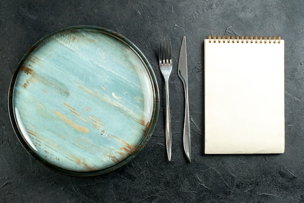 Vue de dessus plateau rond fourchette en acier et cahier de couteau à dîner sur table noire