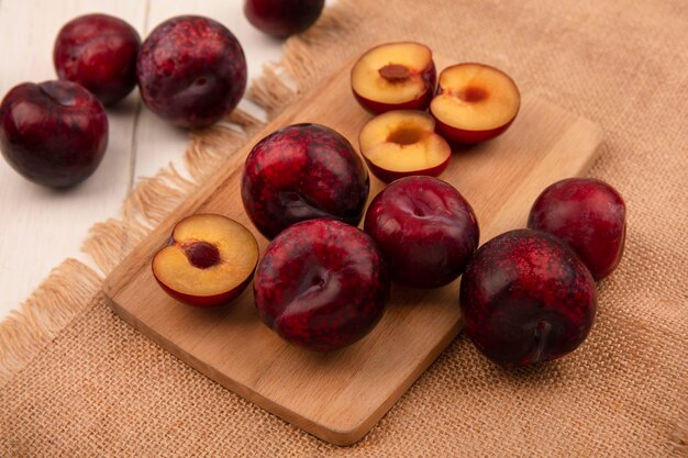 Vue de dessus des pluots frais isolés sur une planche de cuisine en bois sur un tissu de sac sur un fond en bois beige