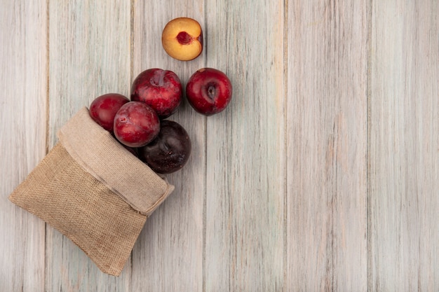 Vue de dessus des pluots juteux et sucrés tombant du sac de jute sur une surface en bois gris avec espace de copie