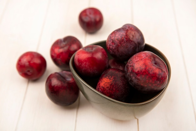 Photo gratuite vue de dessus des pluots à peau rouge foncé sur un bol avec des pluots isolés sur une surface en bois beige