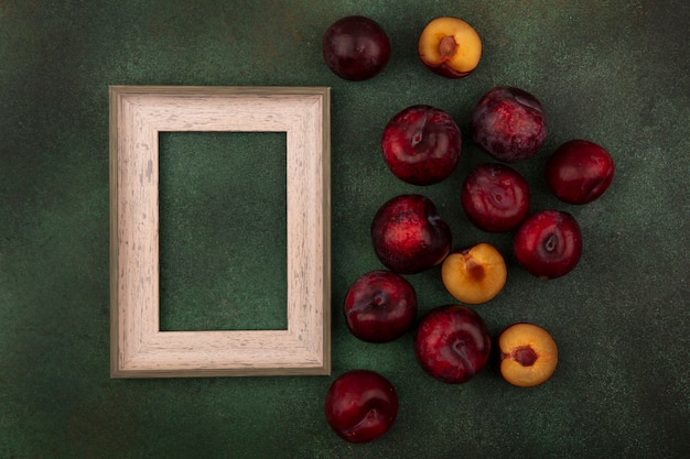 Photo gratuite vue de dessus des pluots à peau rouge foncé doux isolés sur fond vert avec espace copie