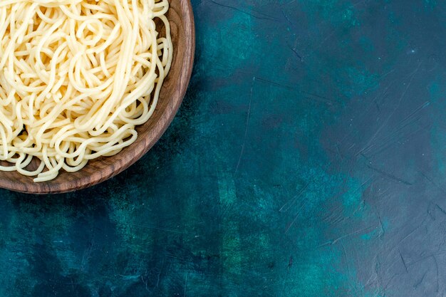 Vue de dessus de plus près des pâtes italiennes cuites à l'intérieur de la plaque en bois ronde sur la surface bleue pâtes italie nourriture dîner pâte viande