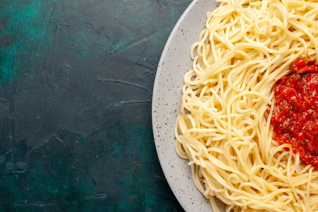 Vue de dessus de plus près des pâtes italiennes cuites avec de la viande hachée et de la sauce tomate sur la surface bleu foncé