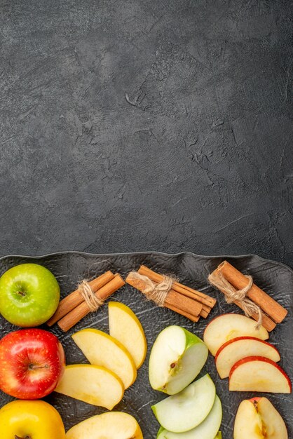 Vue de dessus de plusieurs types de pommes fraîches tranchées et entières sur un plateau noir et citrons verts à la cannelle sur fond sombre