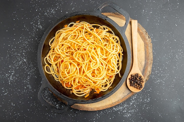 Vue de dessus poêle à spaghetti poivre noir dans une cuillère en bois sur planche de bois sur fond sombre