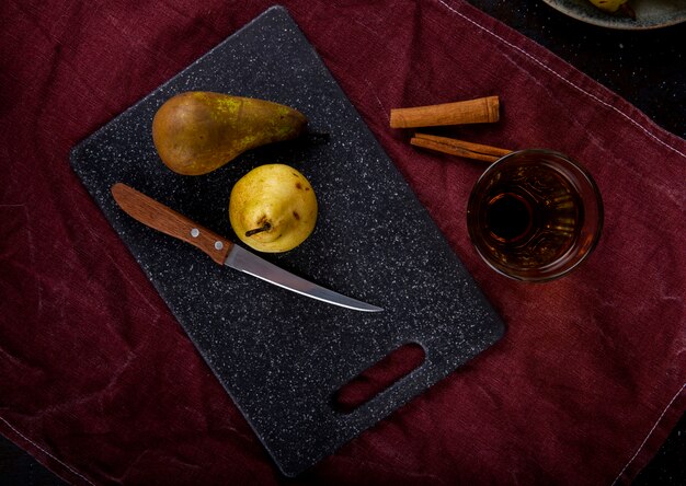 Vue de dessus des poires mûres sur un tableau noir avec un couteau de cuisine et un verre de jus sur une nappe violette