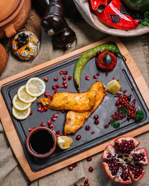 Vue de dessus de poisson grillé à la tomate et au piment grillé avec des tranches de citron à la grenade et de la sauce narsharab