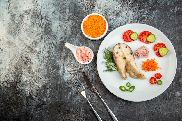 Vue de dessus des poissons crus et des aliments frais hachés de poivre sur une plaque blanche et des couverts sur la surface de la glace