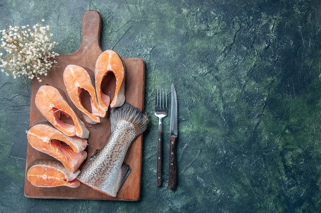 Vue de dessus de poissons crus frais sur une planche à découper en bois et un couteau sur le côté droit sur la table de couleurs de mélange sombre avec de l'espace libre
