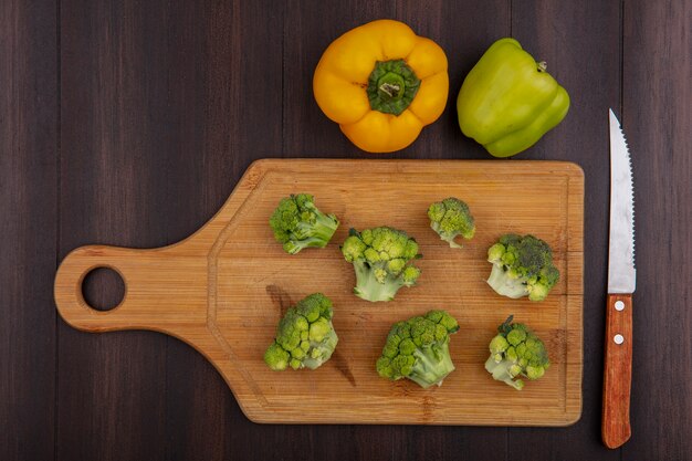 Vue de dessus poivrons colorés avec du brocoli sur une planche à découper avec un couteau sur fond de bois