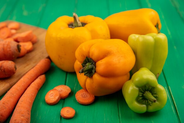 Vue de dessus des poivrons colorés frais avec des carottes isolés sur un mur en bois vert