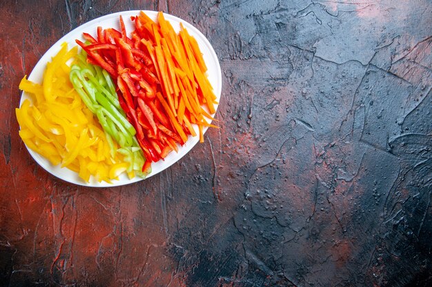 Vue de dessus poivrons coupés colorés sur plaque blanche sur table rouge foncé avec place libre