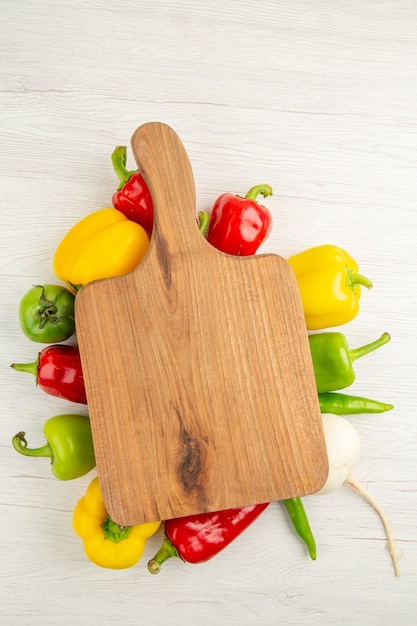 Vue de dessus des poivrons frais de différentes couleurs avec un bureau en bois marron sur fond blanc salade mûre photo couleur repas